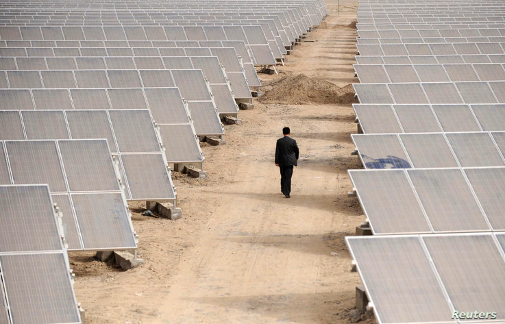 A man walks through solar panels at a solar power plant under construction in Aksu, Xinjiang Uyghur Autonomous Region April 5,…