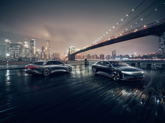 Two Lucid Air luxury sedans under a city bridge at night. 