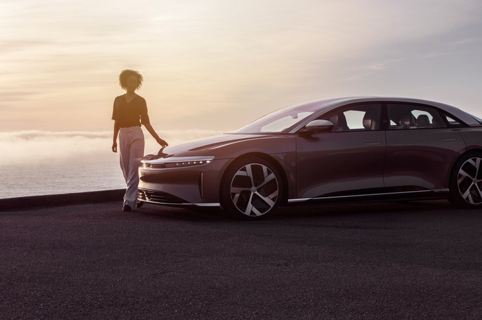 A person touches the hood of the Lucid Air luxury sedan in front of a background of crashing waves. 