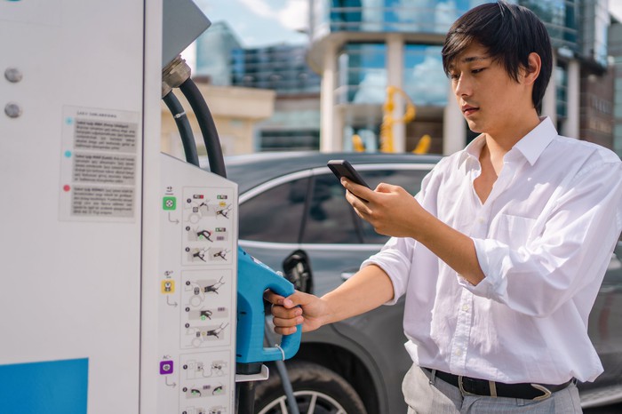 Young man charging an electric car at public charging station.
